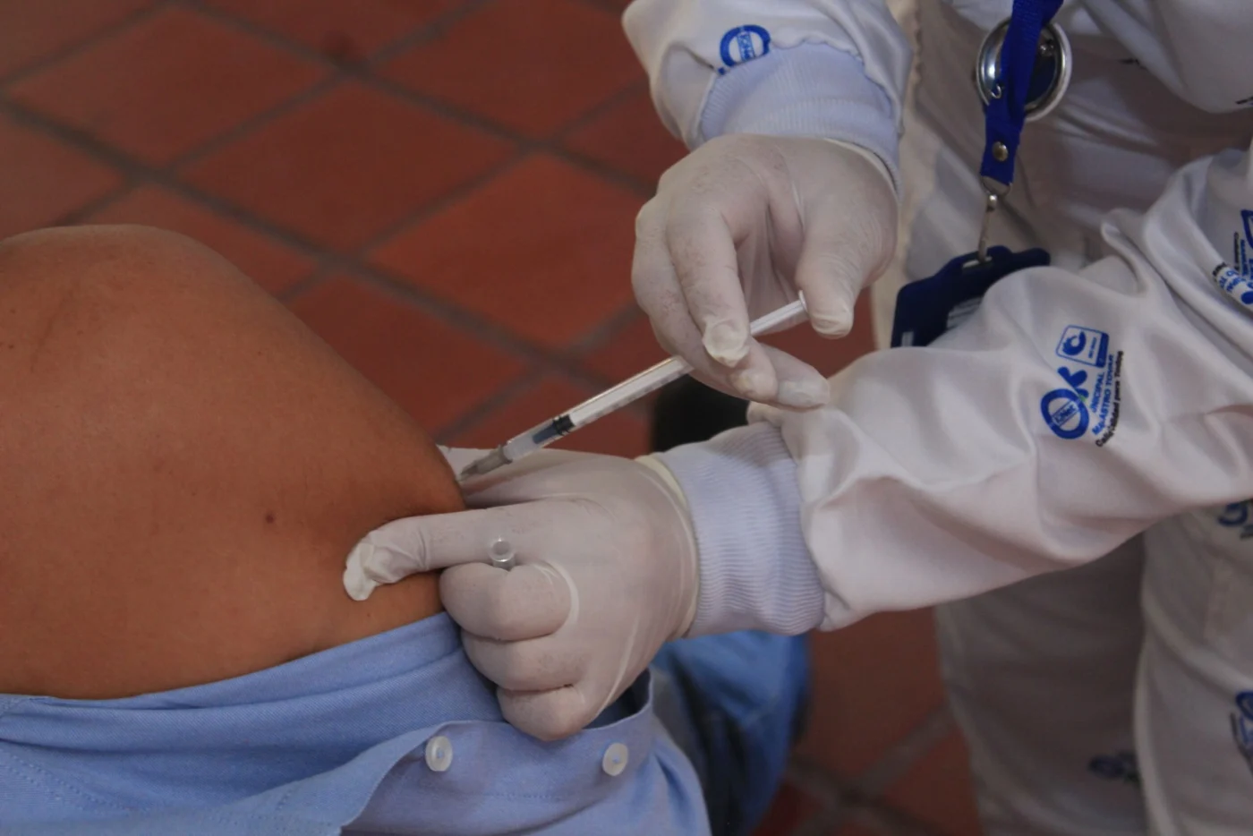 Healthcare worker in gloves administering a flu vaccine injection to a patient's arm in a clinical setting
