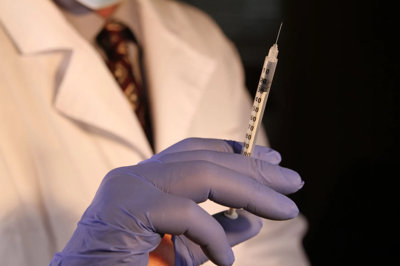 Healthcare professional in blue gloves holding a prepared syringe for a vaccination