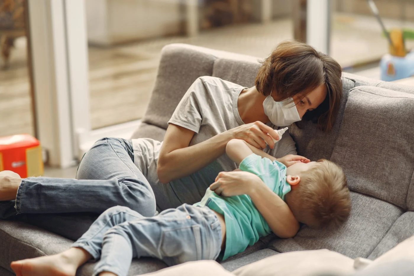 Mother comforting her young son at home while giving him nasal drops for congestion relief