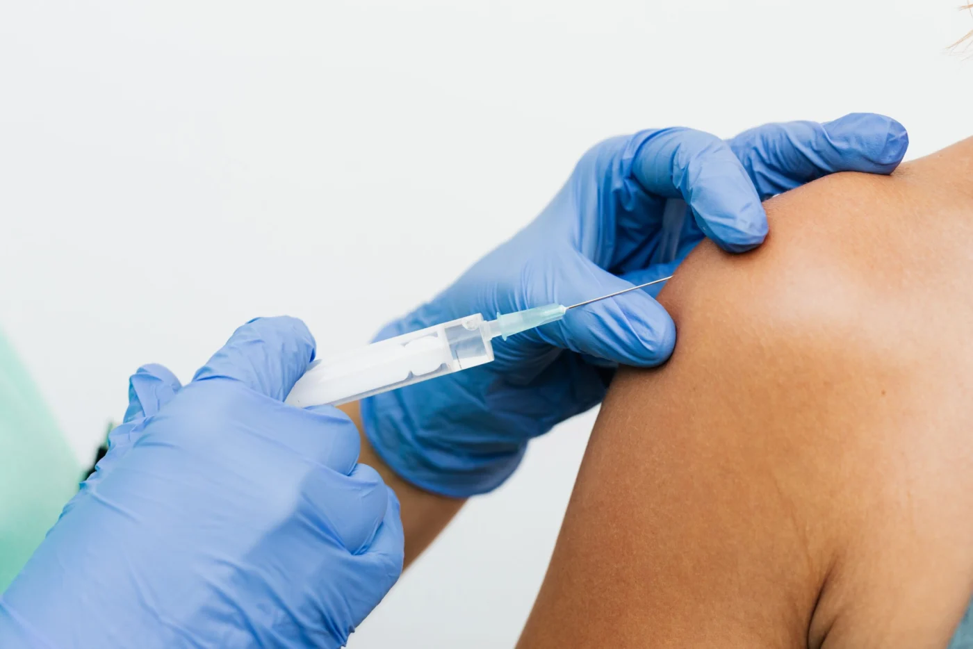 Healthcare worker in blue gloves administering a vaccine injection into a patient's arm in a clinical setting