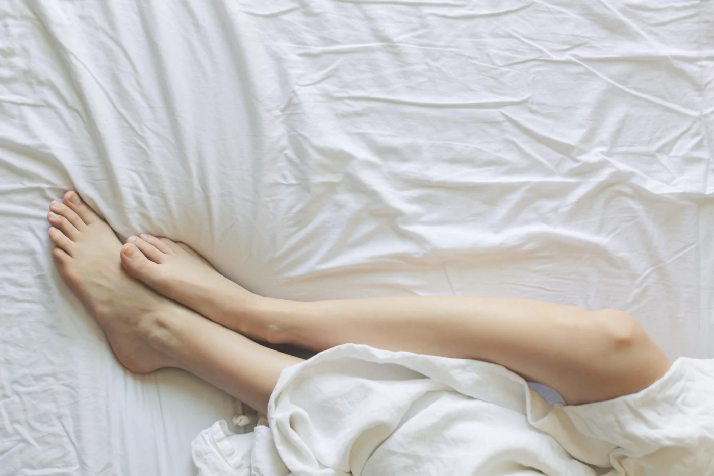 Person resting comfortably under soft white bedding at home