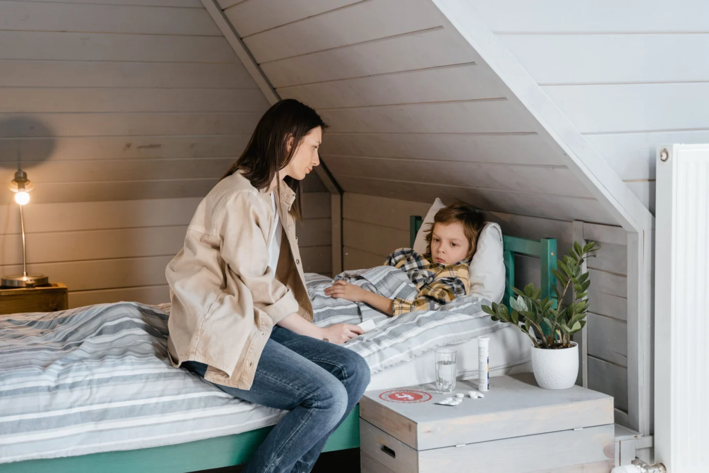 Mother gently caring for her young child tucked in bed, side view in a cozy bedroom